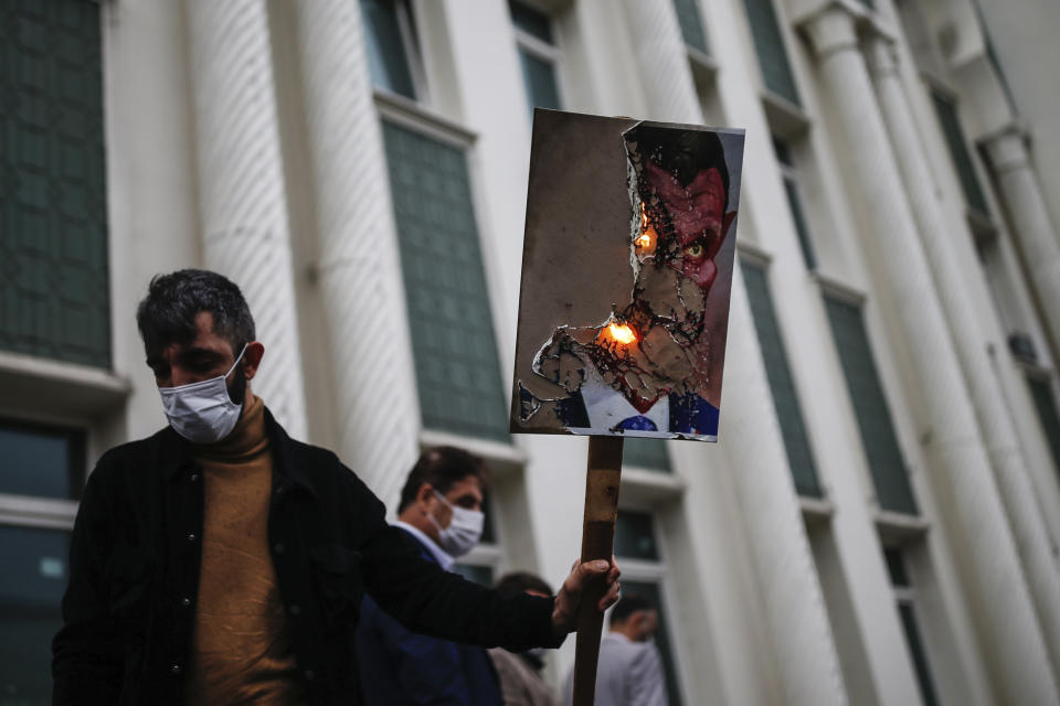 A man holds a poster with a caricature of France's President Emmanuel Macron, depicting him as a devil, which was set on fire, during a protest against France in Istanbul, Friday, Oct. 30, 2020. There is ongoing tension between France and Turkey after Turkish President Recep Tayyip Erdogan said Macron needed mental health treatment and made other comments that the French government described as unacceptably rude. Erdogan questioned his French counterpart's mental condition while criticizing Macron's attitude toward Islam and Muslims. (AP Photo/Emrah Gurel)