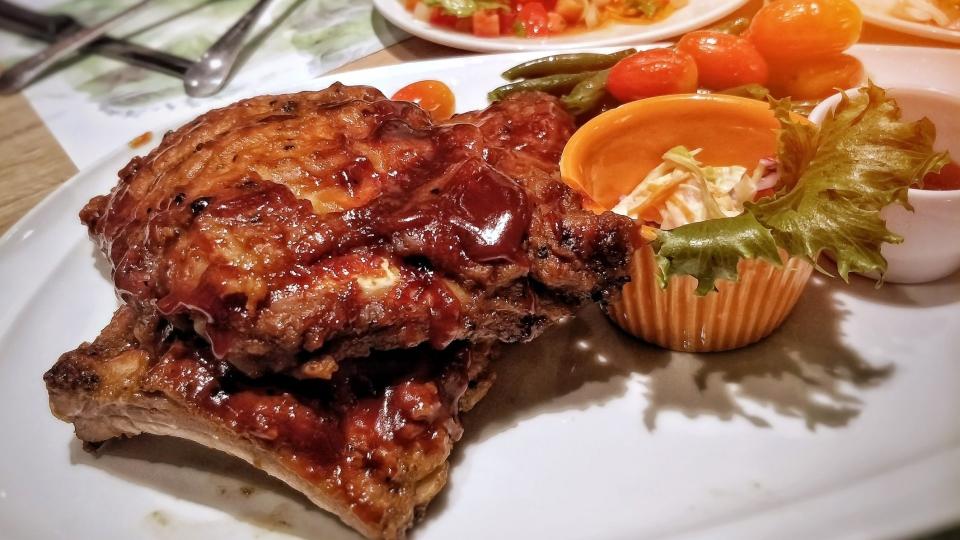 restaurant environment - honey pork rib steak with herb served on white plate dish with fresh salad in background.