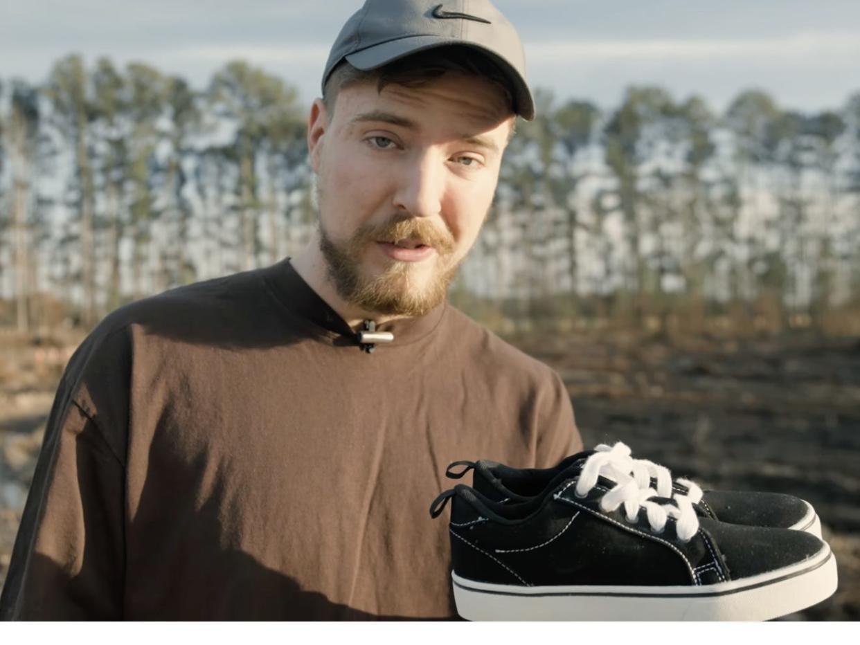 MrBeast in front of a field holding up a pair of black sneakers.