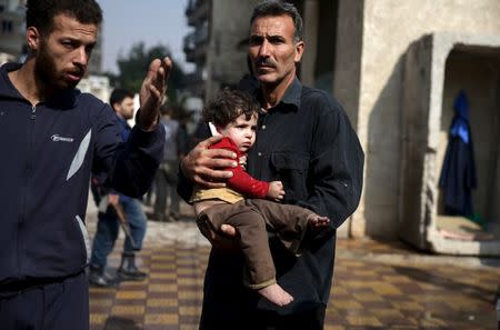 A man carries an injured child as another man gestures at a site hit by missiles fired by Syrian government forces on a busy marketplace in the Douma neighborhood of Damascus, Syria October 30, 2015. REUTERS/Bassam Khabieh