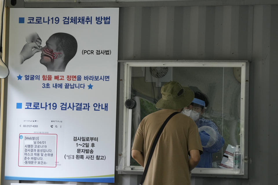 A medical worker in a booth takes a nasal sample from a man at a coronavirus testing site in Seoul, South Korea, Tuesday, July 6, 2021. The sign at left reads: "How to collect COVID-19 samples." (AP Photo/Ahn Young-joon)
