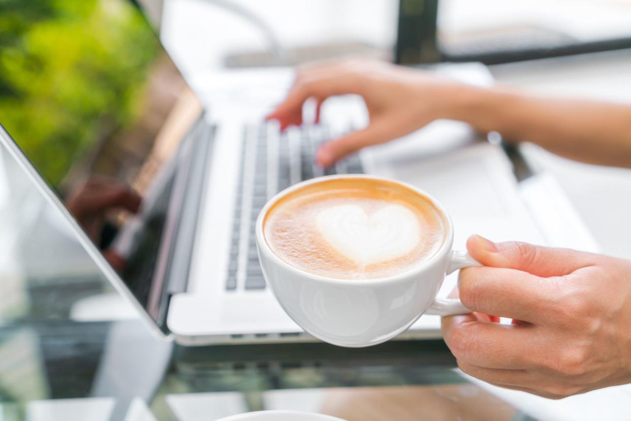 hand holding latte with heart while at a cafe using laptop