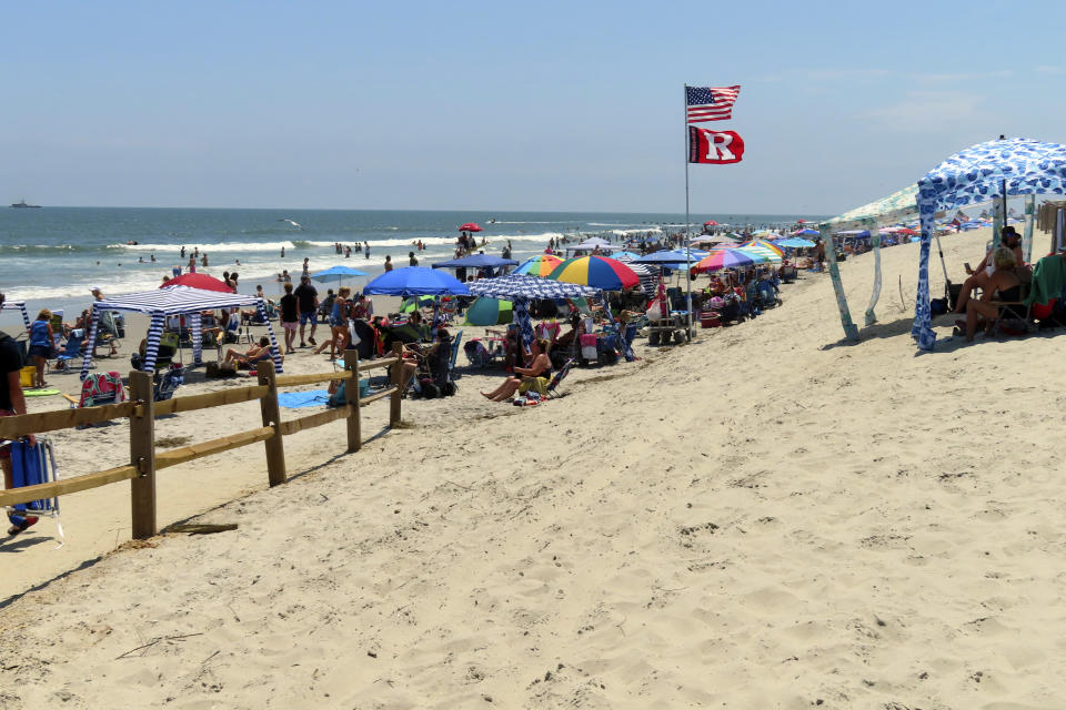 Beachgoers line the sand in North Wildwood, N.J., Friday, July 7, 2023, including -- illegally -- atop what is left of a sand dune, right, that has been repeatedly reshaped by the city, often without state permission. New Jersey has fined North Wildwood $12 million for unauthorized dune reshaping, but the city says it acted during emergencies to protect ots shoreline. The dune shown in this photo is about 70% smaller than it was in May, before two recent emergency projects by the city to reshape it. (AP Photo/Wayne Parry)