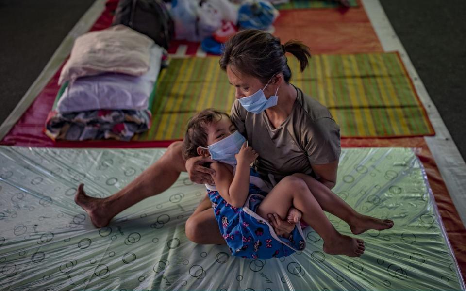 A homeless child and her mother wearing facemasks rest inside a gymnasium converted into a shelter for the homeless who are unable to feed themselves and unable to work because of government lockdown measures - Getty Images AsiaPac 