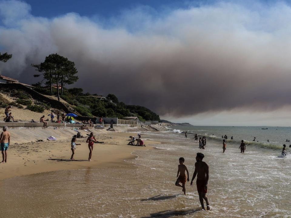 Dark smoke is shown floating over a sunny beach in Teste-de-Buch forest rises from the Dune of Pilat in the background, in the Arcachon basin southwest France, on July 13, 2022