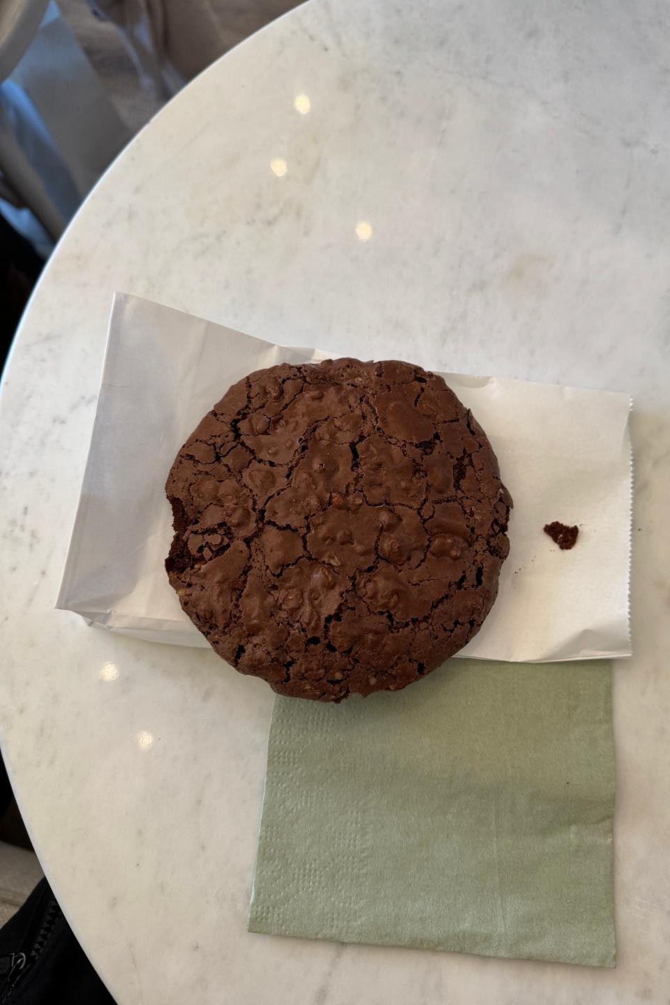 A cracked chocolate cookie rests on a white napkin atop a green napkin, arranged on a marble table