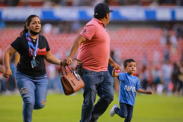 QUERETARO, MEXICO - MARCH 05: A family runs through the field after fans started a fight during the 9th round match between Queretaro and Atlas as part of the Torneo Grita Mexico C22 Liga MX at La Corregidora Stadium on March 05, 2022 in Queretaro, Mexico. The match was suspended on the 60th minute due to violent fights between fans resulting in many injured. (Photo by Manuel Velasquez/Getty Images)