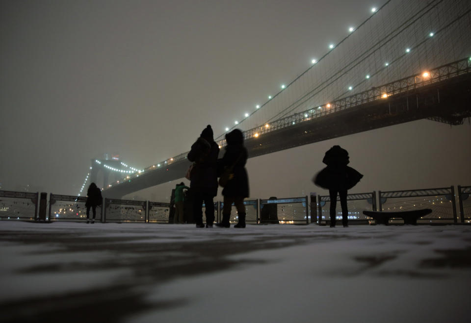 FILE - This Jan. 2, 2014 file photo shows visitors on the waterfront in Brooklyn to photograph the Brooklyn Bridge during a winter storm in New York. If you don’t mind the cold, walking across the Brooklyn Bridge is a classic New York City outing for tourists, one of a number of things Super Bowl visitors might consider doing when they’re in town for the big game. (AP Photo/Peter Morgan, File)
