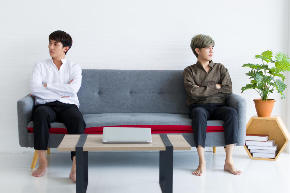 Gay couple sitting on the sofa bed with arms crossed and don't look at each other. 