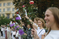 Belarusian opposition supporters hold flowers and flash victory signs during a protest in Victory Square in Minsk, Belarus, Thursday, Aug. 20, 2020. Demonstrators are taking to the streets of the Belarusian capital and other cities, keeping up their push for the resignation of the nation's authoritarian leader. President Alexander Lukashenko has extended his 26-year rule in a vote the opposition saw as rigged. (AP Photo/Sergei Grits)