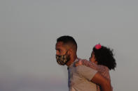 A child gets a piggy back ride from her father as the sun begins to set in Cruzeiro Square in Brasilia, Brazil, Friday, July 31, 2020. People gathered outdoors in the late afternoon as authorities eased the restrictions related to the new coronavirus, despite that Brazil's official COVID-19 death toll is the second highest in the world after the United States. (AP Photo/Eraldo Peres)