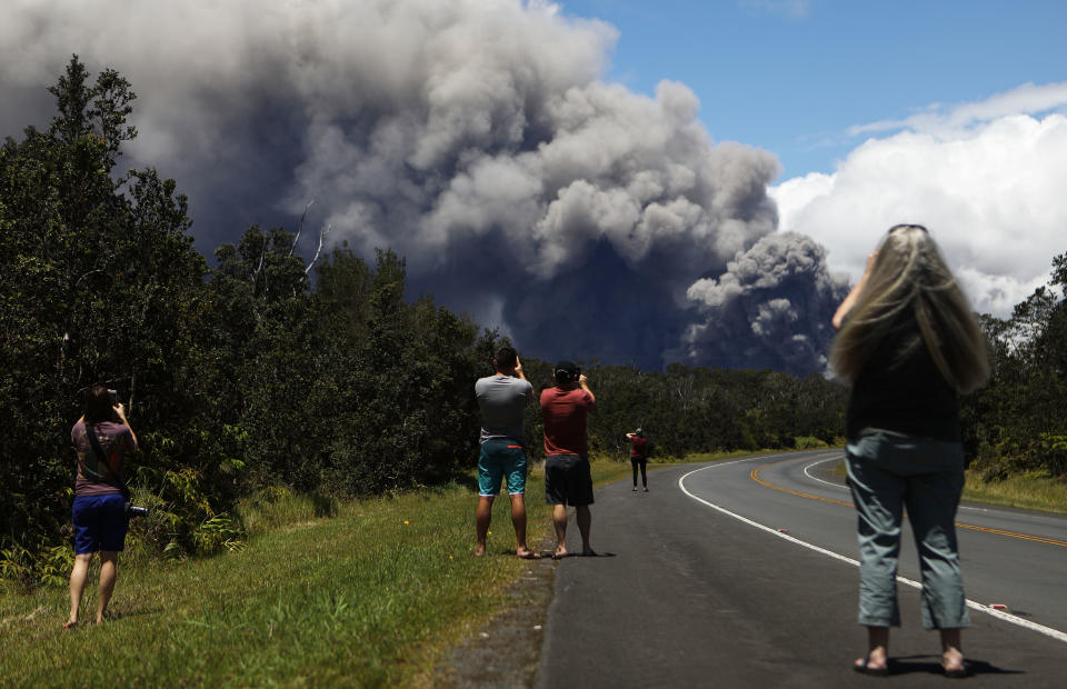 <p>Locals are seen on the side of the road as smoke billows from the huge eruption (Getty) </p>