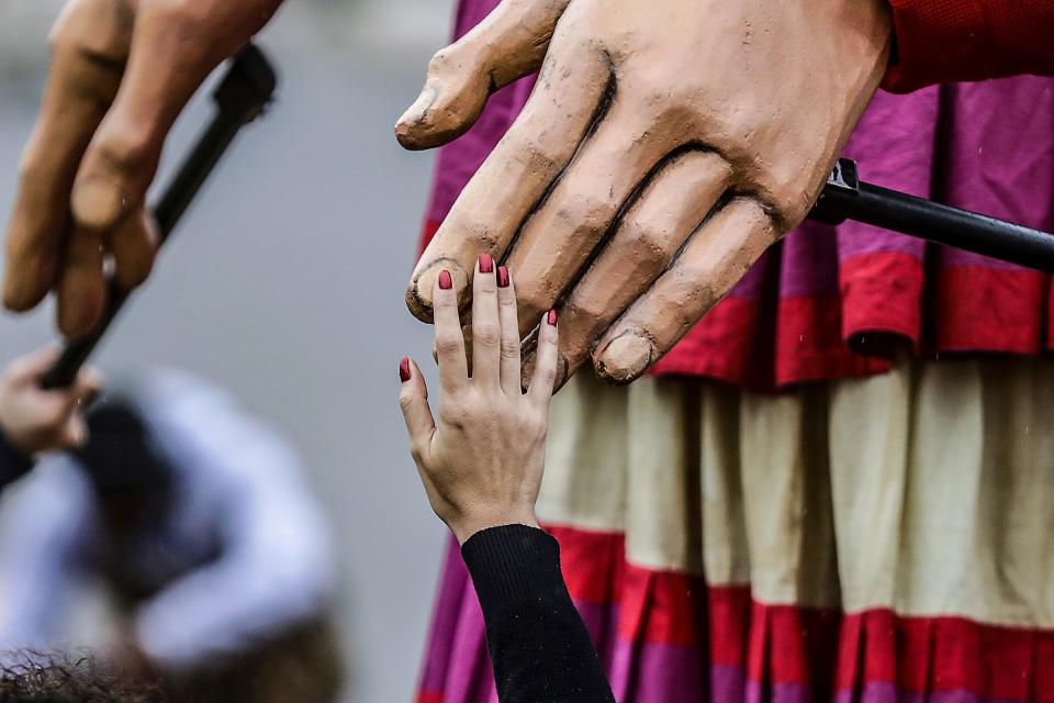 An onlooker reaches out to touch the hand of Little Amal, a 12-foot-tall puppet of a 10-year-old Syrian refugee girl that traveled to Detroit as a symbol of displaced people across the globe in southwest Detroit on Wednesday, Sept. 27, 2023.