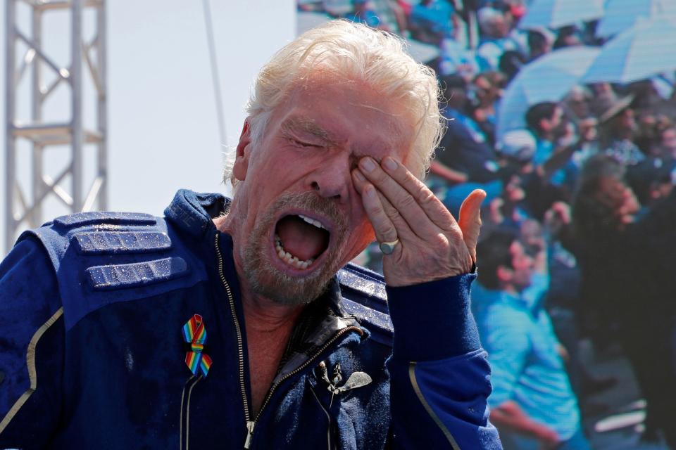Richard Branson wipes his eye, with a rocket platform in the background.