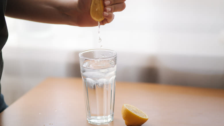 Hand squeezing lemon juice into glass of water
