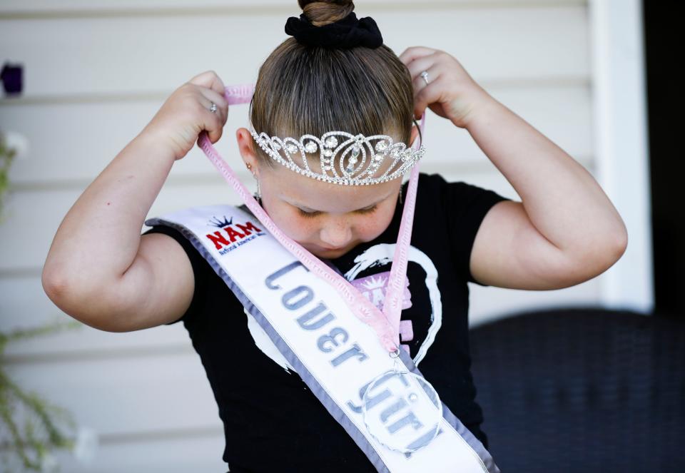 Six-year-old Bentlee Graham puts on one of her awards she won in the National American Little Miss Missouri pageant in July.