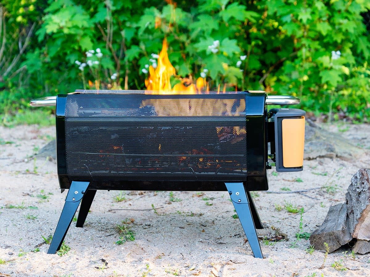 BioLite FirePit Plus burning wood in sand pit near green shrubs