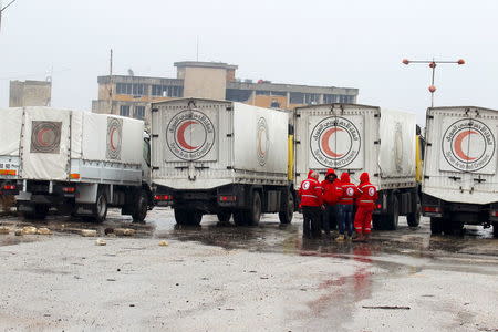 Red Crescent workers stand near their vehicles prior to inspection from rebels before heading to al Foua and Kefraya, in Idlib province, Syria January 11, 2016. REUTERS/Ammar Abdullah