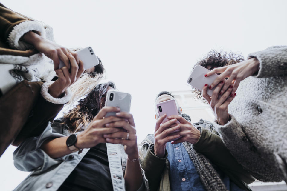 Four people standing close using smartphones