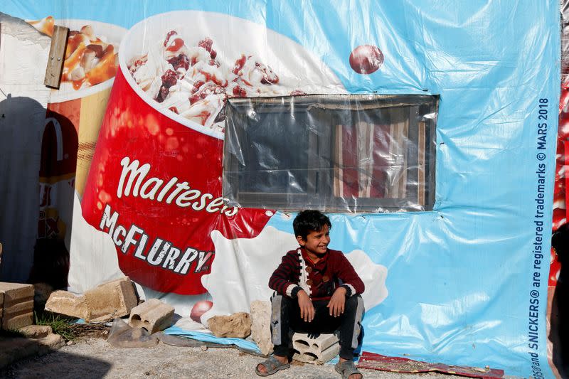 FILE PHOTO: A Syrian refugee boy sits outside a tent at a camp in Bar Elias