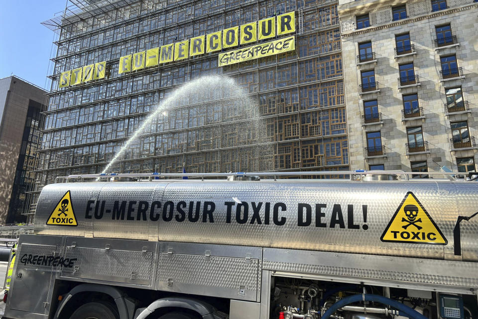A Greenpeace activist sprays water to simulate pesticide spray toward the European Council building, outside of a meeting of EU trade ministers, in Brussels, Thursday, May 25, 2023. The European Union Trade Ministers meet in Brussels Thursday to discuss, among other issues, the state of play of the trade relations with the United States and recent developments in EU-China trade relations. (AP Photo/Sylvain Plazy)