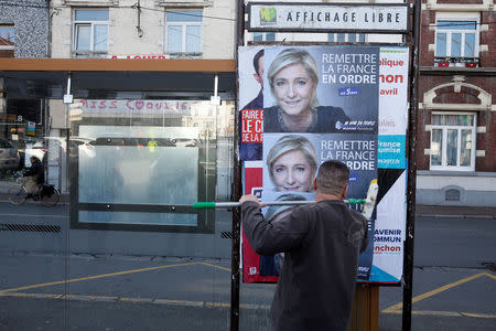 A member of the National Front party pastes a poster on a free billboard for French far right National Front political party leader Marine Le Pen as part of the 2017 French presidential election campaign in Henin-Beaumont, France, April 6, 2017. REUTERS/Pascal Rossignol