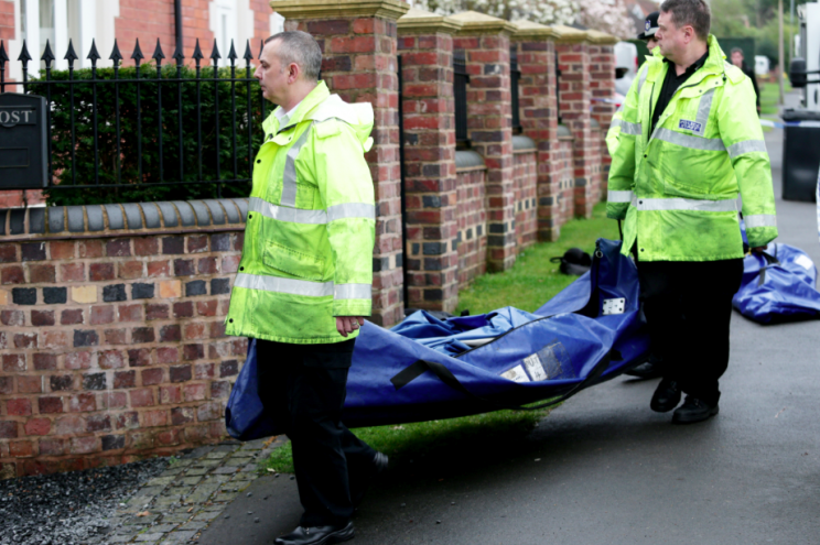 Police remove a body from the house where three people were stabbed (SWNS)