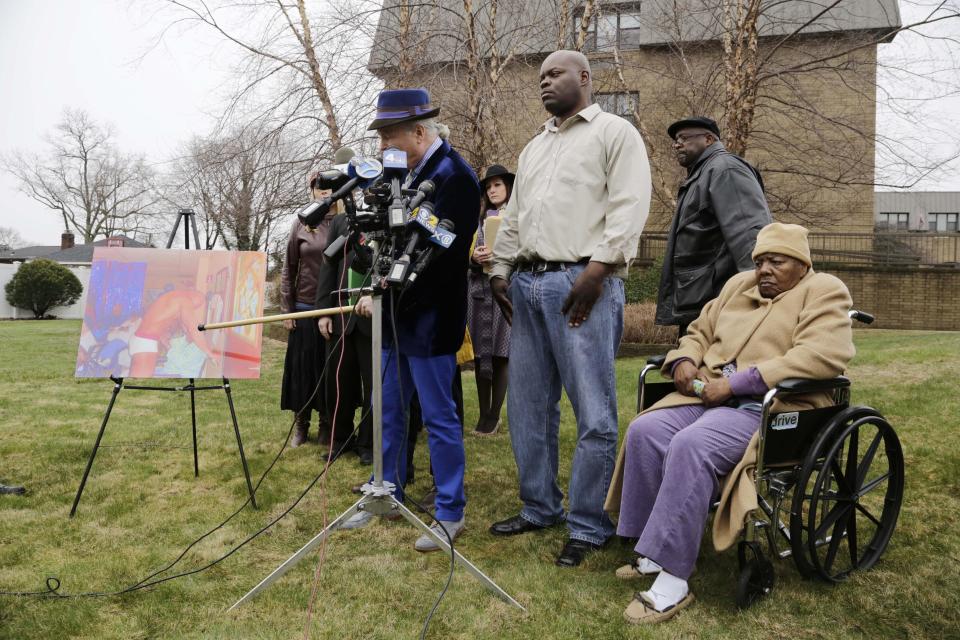 Bernice Youngblood, right, 85, a resident of the East Neck Nursing and Rehabilitation Center, listens as her attorney, John Ray, left, points to a photograph with his cane during a news conference on the lawn of the nursing home, Tuesday, April 8, 2014 in West Babylon, N.Y. The photograph reportedly shows a male exotic dancer performing for Youngblood and other patients at the facility. With Youngblood are her sons, Darrell, center, and Franklin, second right. (AP Photo/Mark Lennihan)