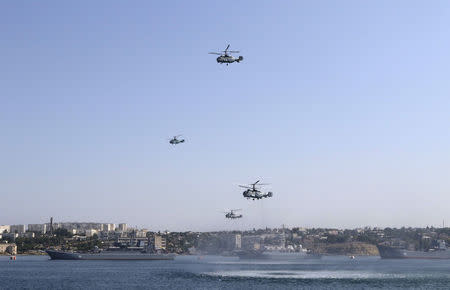 Russian military helicopters fly in formation, with warships seen on the water, during celebrations for Navy Day in the Black Sea port of Sevastopol, Crimea, July 26, 2015. REUTERS/Pavel Rebrov/File Photo