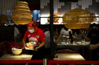 An employee wearing a face mask to protect against the coronavirus clears a table at a restaurant in a shopping mall in Beijing, Friday, Aug. 14, 2020. China's factory output rose just under 5% last month from a year earlier while retail sales fell slightly, suggesting the country's recovery from the coronavirus pandemic remains muted. (AP Photo/Mark Schiefelbein)