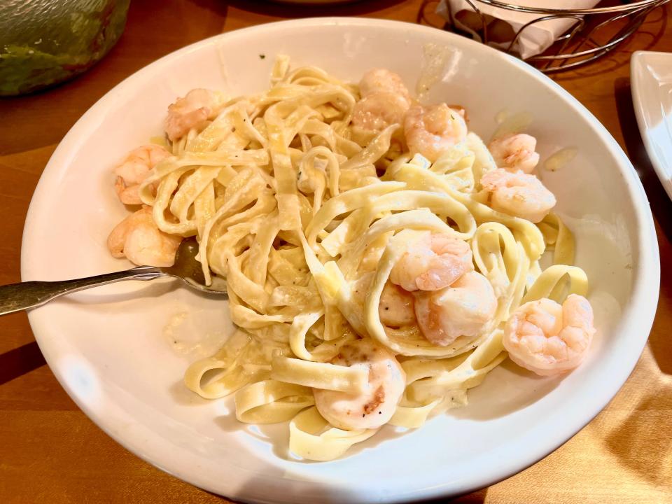 White bowl of cream-covered fettuccine with shrimp on a brown table at Olive Garden