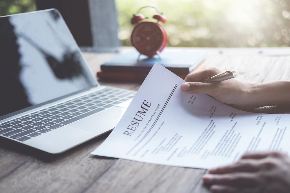 A person holds their resume as they prepare to work on their laptop