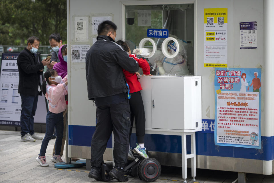 A worker in a protective suit swabs a child's throat for a COVID-19 test at a testing site in Beijing, Thursday, April 28, 2022. Beijing shifted more classes online Thursday in a further tightening of COVID-19 restrictions, as China's capital seeks to prevent a wider outbreak. (AP Photo/Mark Schiefelbein)