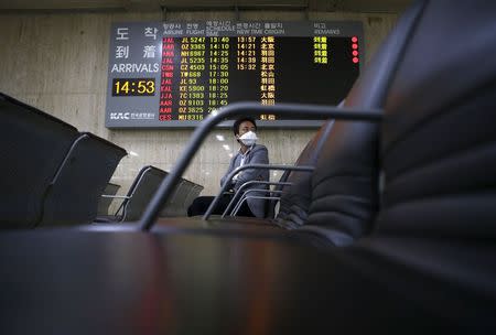 A passenger wearing masks to prevent contracting Middle East Respiratory Syndrome (MERS) sits in front of an arrivals signboard at Gimpo International Airport in Seoul, South Korea, June 17, 2015. REUTERS/Kim Hong-Ji