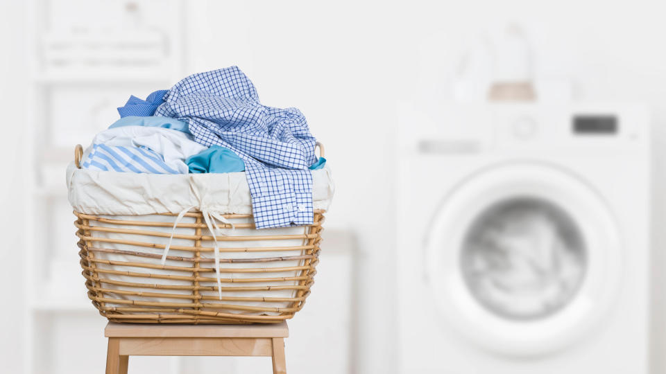 A hamper filled with dirty laundry in front of a washing machine