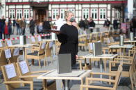 Waitress Alin Lepetit stands in the outdoor area of a café on the market square during an action to open the outdoor gastronomy, Wernigerode, Germany, Wednesday, March 3, 2021. Behind her, passers-by watch from behind a barrier tape. Numerous businesses also took part in the action nationwide. (Matthias Bein/dpa via AP)
