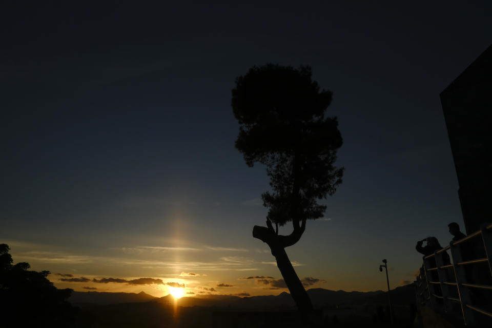 People stand close to a tree as the sun sets on a spring evening, in Pamplona, northern Spain, Wednesday, May 19, 2021. (AP Photo/Alvaro Barrientos)