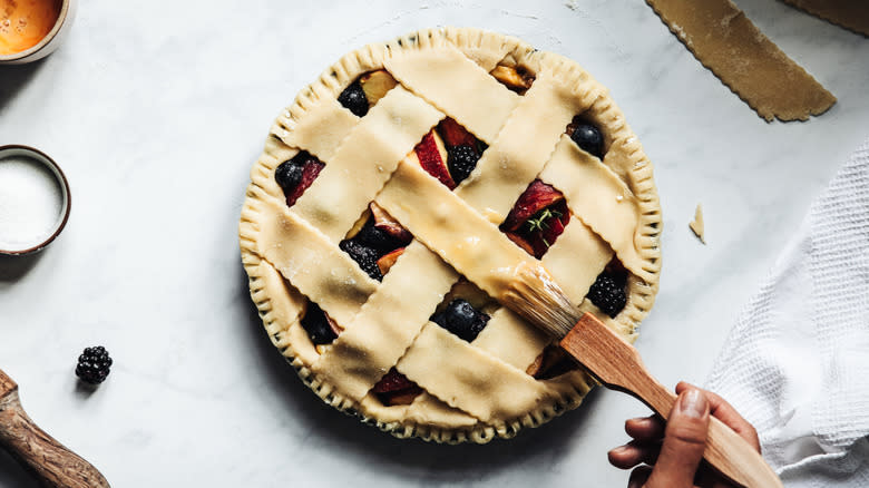 Hand applying egg wash on lattice-top pie