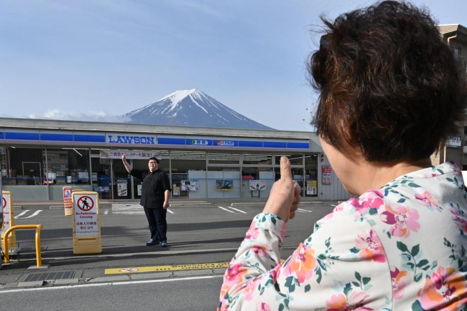 A person takes pictures of Mount Fuji from across the street of a convenience store, hours before the installation of a barrier (AFP via Getty Images)