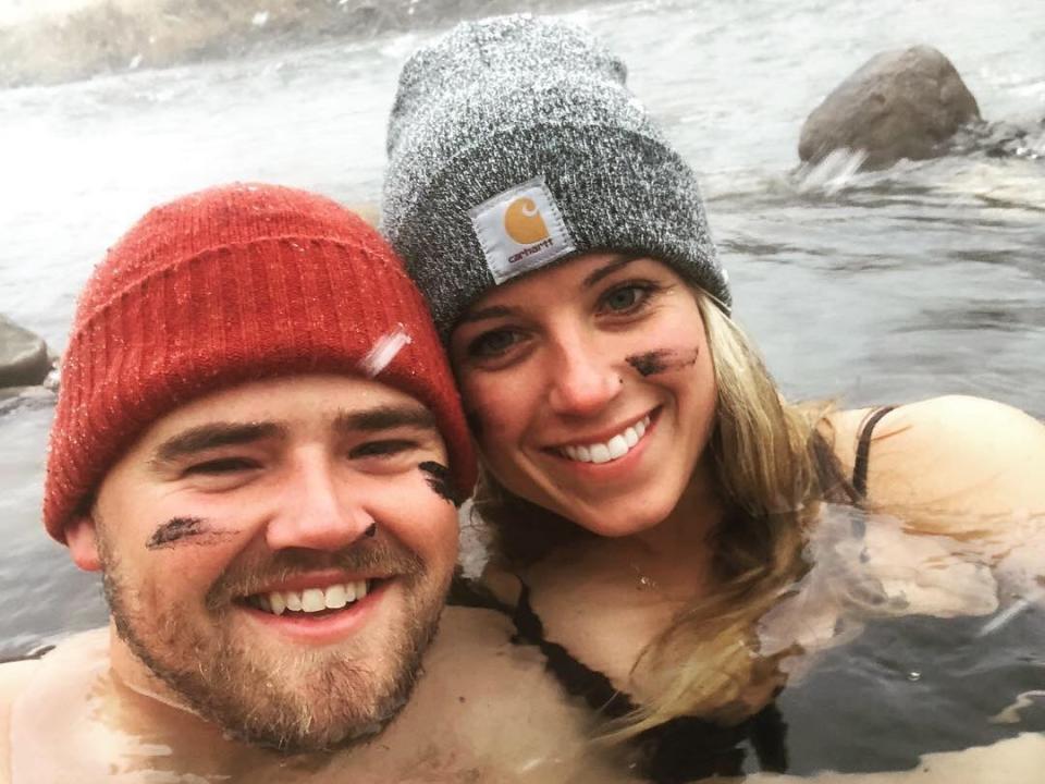 A woman and a man wearing beanies sitting in a hot spring with two stripes on their cheeks.