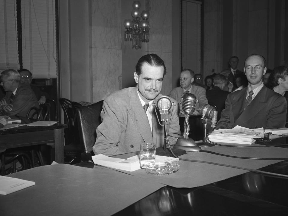 Howard Hughes speaks into microphones as he testifies that he did not offer to pay $100,000 if he could persuade New York officials to relax their ban against the motion picture The Outlaw.