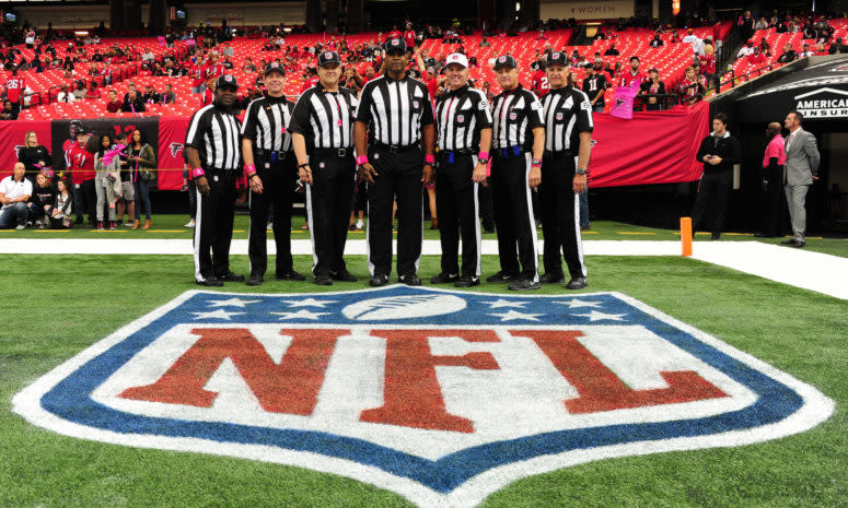 Bill Vinovich and other referees stand on field around NFL logo before a game.