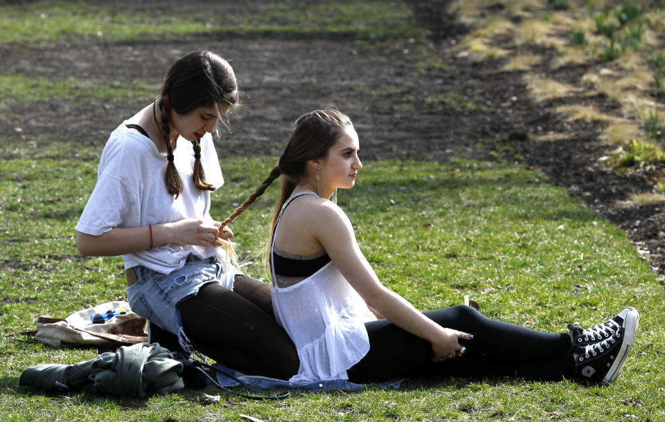 Alana Handman, left, from Atlanta, braids the hair of fellow Columbia College student, Sarah Genematis, from Detroit, Mich., in Chicago's Millennium Park, Tuesday, March 13, 2012. Temperatures were close to record highs after a mild winter on Tuesday. (AP Photo/Charles Rex Arbogast)