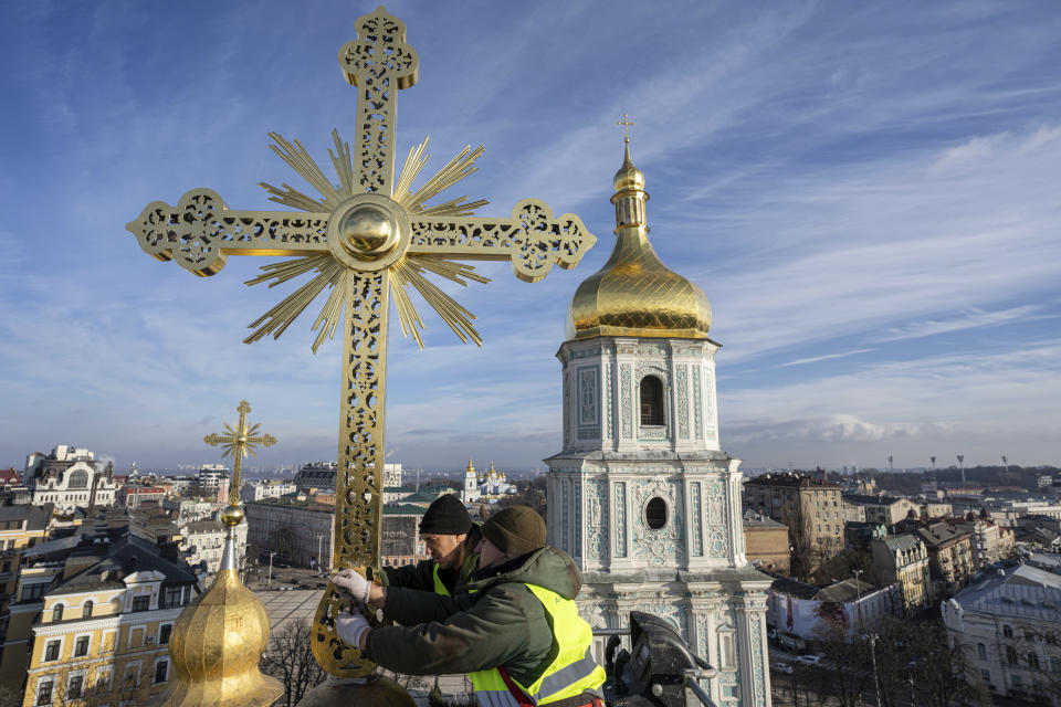 Ihor Kuzmenko, left, and Yuriy Maliuh altitude workers install a restored cross on a dome of Saint Sophia Cathedral in Kyiv, Ukraine, Thursday, Dec. 21, 2023. A UNESCO World Heritage site, the gold-domed St. Sophia Cathedral, located in the heart of Kyiv, was built in the 11th century and designed to rival the Hagia Sophia in Istanbul. (AP Photo/Evgeniy Maloletka)
