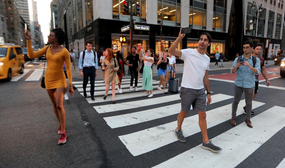 Pedestrians stop on 42nd St. in Manhattan July 11, 2022 to photograph the phenomenon known as Manhattanhenge.
