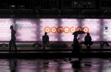 FILE PHOTO: People sit at a bus station with an Ooredoo advertisement as they wait for a bus in Yangon August 1, 2014. REUTERS/Soe Zeya Tun/File Photo