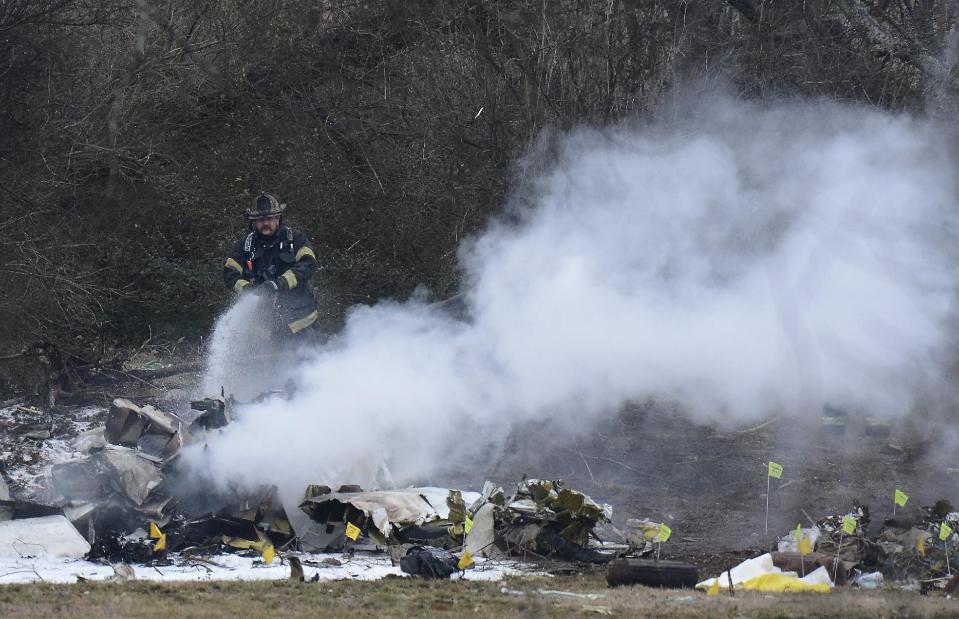 A Nashville fire department firefighter extinguishes a small fire at the crash site on Tuesday, Feb. 4, 2014 near Nashville. The small plane crashed on Monday, near a YMCA in suburban Nashville, killing everyone on board and damaging cars in the parking lot. (AP Photo/Mark Zaleski)