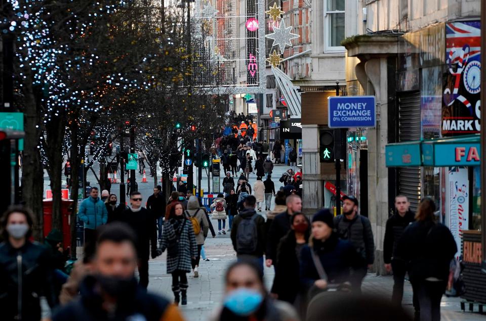 Pedestrians, some wearing a face mask or covering due to the COVID-19 pandemic, walk past closed shops in central London on December 20, 2020.