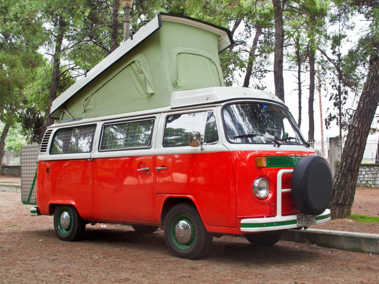 A loaded up vintage, orange and white Volkswagen bus is parked at a resting point during a road trip