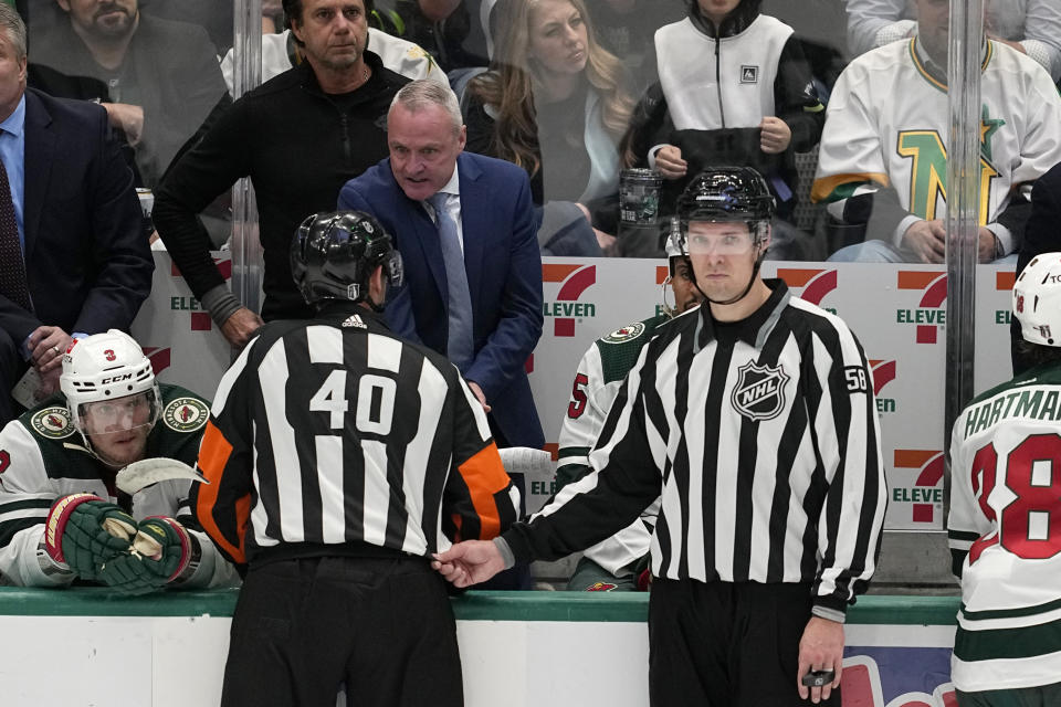 Minnesota Wild head coach Dean Evason, center in blue coat, talks to referee Steve Kozari (40) and linesman Ryan Gibbons (58) late in the third period of Game 5 of an NHL hockey Stanley Cup first-round playoff series against the Dallas Stars, Tuesday, April 25, 2023, in Dallas. (AP Photo/Tony Gutierrez)